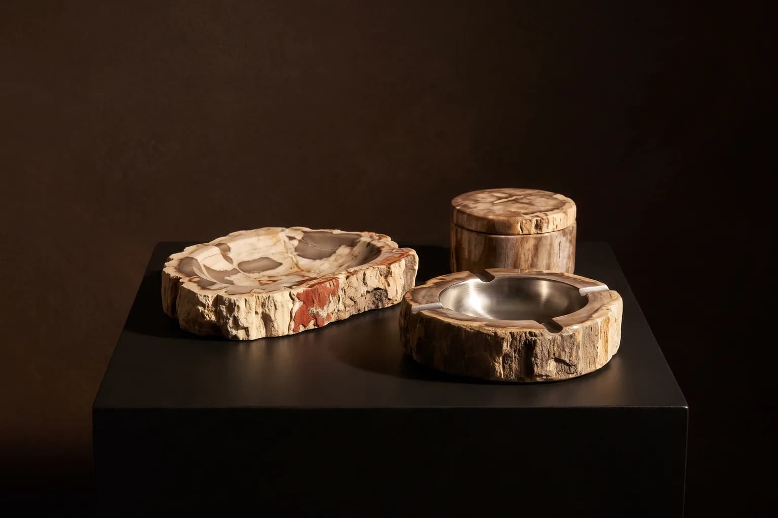 Visualisation éditoriale d'un vide-poche, d'un cendrier et d'une boîte en bois pétrifié groupés sur un socle noir
