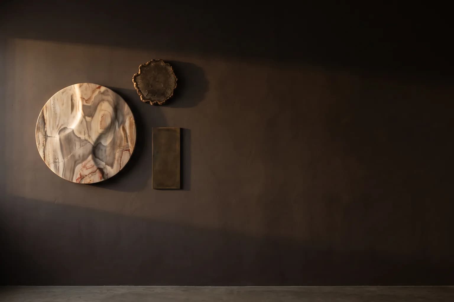 Visualisation éditoriale de trois pièces murales, un bas-relief poli, un disque minéral brut et une plaque de bronze patiné
