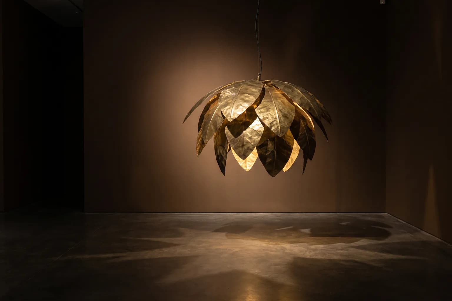 Visualisation éditoriale d'une suspension en laiton martelé formant une canopée qui projette une lumière tachetée au sol