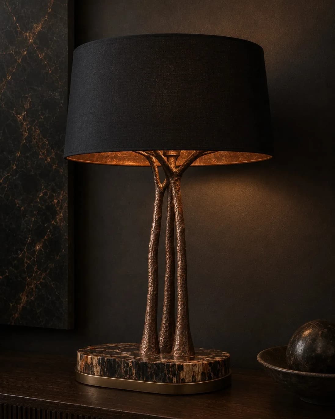 Photographie d'un luminaire MEDUSA : sous un abat-jour sombre doublé de cuivre, trois fûts de bronze martelé s'élèvent d'un socle de marqueterie de bois pétrifié cerclé de laiton